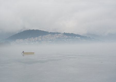 Scene  with yellow boat in frozen lake and a town emerge while the fog partedの写真素材