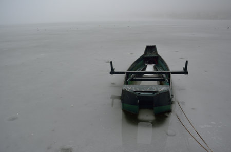 Winter foggy day  in the frozen lake and a wooden boat trapped in icy watersの写真素材