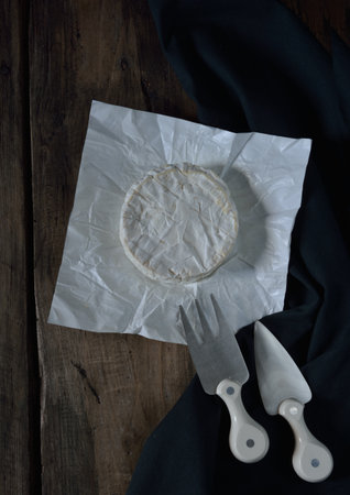 Camembert cheese with cheese fork and cheese knife  on wooden rustic table and black dishtowelの写真素材