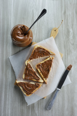 Slice of bread spread with hazelnut praline paste onÂ  a plate and grey table as background