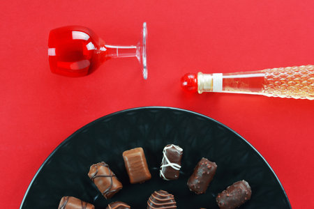 Red glass, a liquor bottle with red cap and black plate with chocolate candies on red backgroundの写真素材