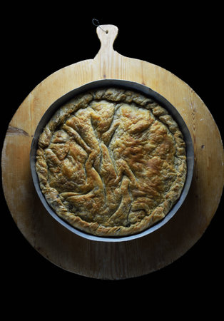Traditional greek spinach cheese pie in baking pan on wooden dough rolling board