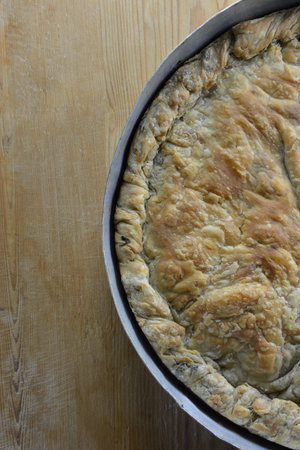 Greek spinach cheese pie in baking pan and wooden table as backgroundの写真素材