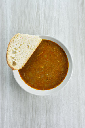 Soup bowl with lentil soup and slice of bread on kitchen tableの写真素材