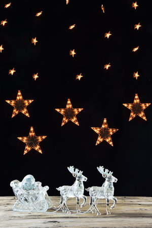 Glass santa claus in sleigh with reindeer ornament and lighting stars as backgroundの写真素材