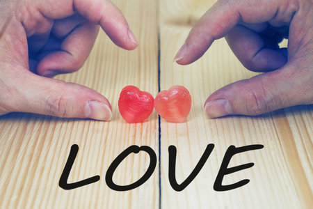 Two Hands will touch heart candy and text "LOVE" on wood plate , valentine day concept.の写真素材