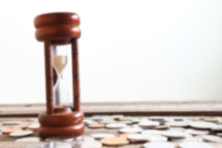 Blur hourglass and coins on wood plate , financial concept