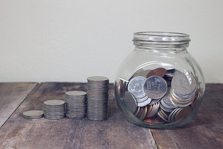 Stack of money and coin in cup glass on wood plateの写真素材