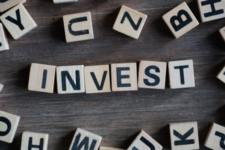 Word INVEST on cube dice on wood table