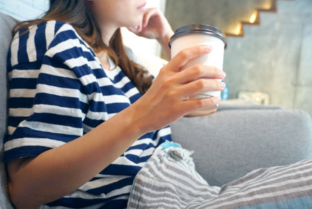 Woman hold coffee cup in right hand and sit on coffee shopの写真素材