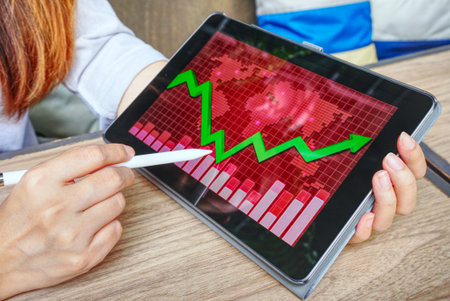 Hand point pen on the screen which have chart and red map data for analysis crisis.