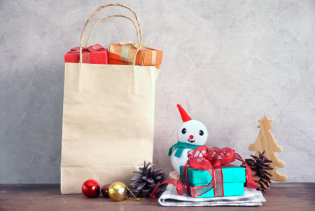Gift boxes in the busket and gift in paper bag and snow man and christmas tree make from wood on wood tableの写真素材