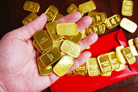 Gold bars on hand with bcakground group of gold bara nad red envelope on the table , chinese new year concept.の写真素材