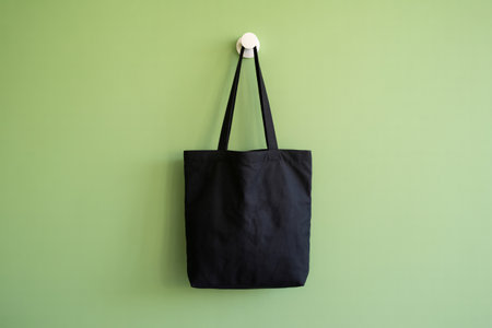 A simple black tote bag hangs from a white hook against a light green wall, showcasing a minimalist and eco-friendly lifestyle choice.の素材