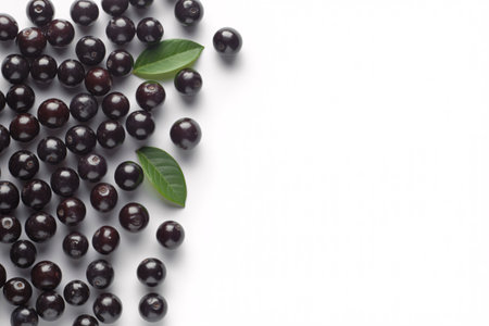 A close-up shot of dark purple acai berries artfully arranged on a clean white surface, accented by two vibrant green leaves.の素材