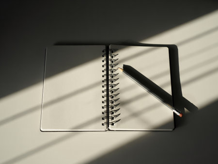 a notebook and pencil sit on a desk with light and shadow, ready for writing or drawing ideasの素材