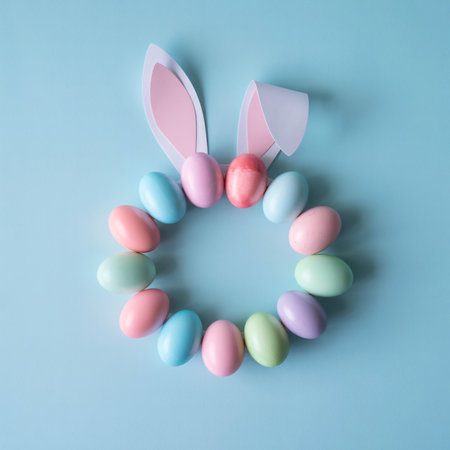 A festive Easter arrangement featuring bunny ears and a circle of pastel-colored eggs on a light blue surface.の素材