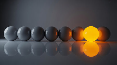 A single bright orange orb illuminates a row of dull gray spheres, representing uniqueness and new ideas.の素材