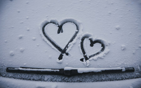 Two hearts drawn on a snow-covered surface with a wiper blade at the bottom, creating a romantic winter scene.の素材