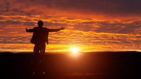 Silhouette of man with his arms raised. A ray of sunshine in the mountains.の写真素材