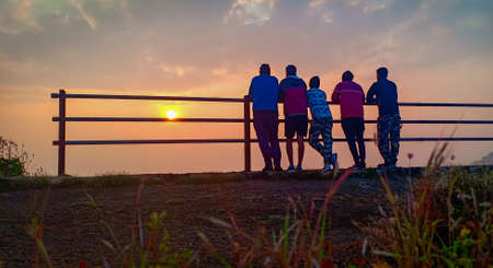 friends looking at sunrise by residing on railingの写真素材