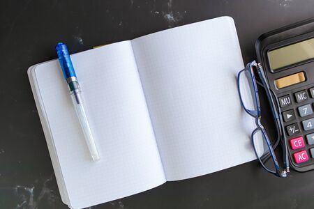 Top view Blank Notebook Calculator and glasses on a black marble table background. Simple financial business concepts, working at home or office for social distancing measures, plus copy space.の写真素材