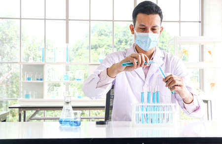 An Asian scientist or chemist drops a blue liquid chemical in a laboratory. Research concepts in...