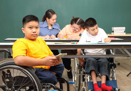 Asian disabled children Or, an autistic child learns to read, write, and train their hand and finger muscles with a teacher at their classroom desk. Concentrate and smile Happy disability kid conceptの写真素材