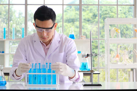 An Asian scientist or chemist drops a blue liquid chemical in a laboratory. Research concepts in...