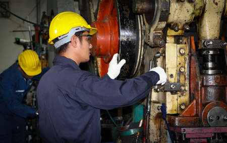 Asian male worker In industries that wear glasses, safety hats and safety uniforms Wrench tool holder stand Machine maintenance technician operation concept In an industrial factory with confidenceの写真素材
