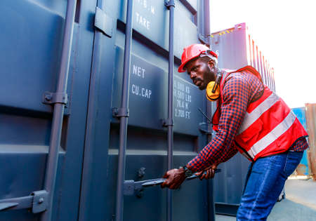Portrait of an African American male employee or supervisor Wearing a safety helmet, opening containers, checking concepts, moving industrial goods, logistics, import-export. commercial transportの写真素材
