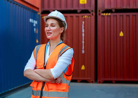 Portrait of a smiling female container employee or foreman wearing a hard hat. White Blurred Box Container Background concept of success and moving industrial products logistics import-exportの写真素材