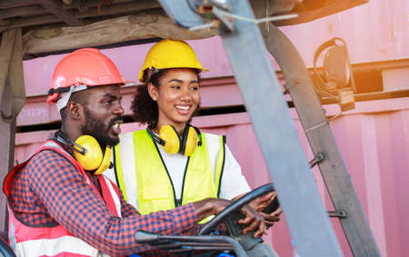 warehouse worker African American men and women In uniform wearing a hat driving a forklift to lift...