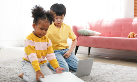 Cute little girls play with Asian boys, use laptops to study together, lounging on the floor in the living room at home. Concept of learning, building development and doing activities together at homeの写真素材