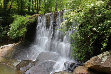 A small waterfall runs smoothly over the rocky edge onto some huge rocks.