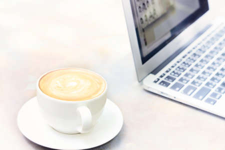 Cappuccino in a white cup with a laptop computerの写真素材