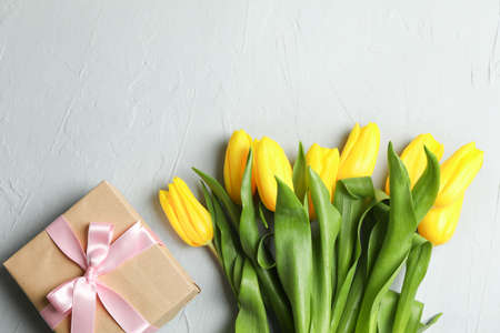 Beautiful bouquet of yellow tulips with gift on grey background, top view. Space for textの写真素材