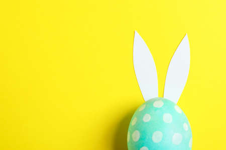Decorated Easter egg with cute bunnies ears on yellow background. Space for textの写真素材