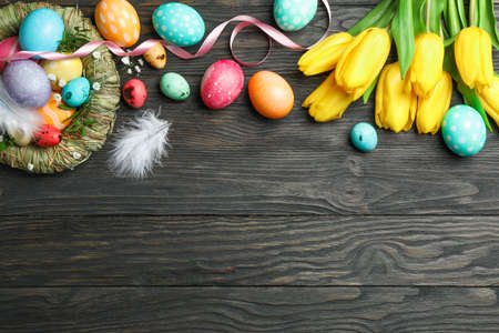 Nest with Ñolorful easter eggs, flowers and feathers on wooden background. Festive tradition....
