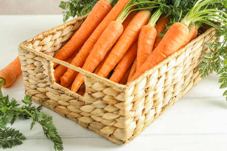 Wicker basket with ripe carrots on wooden table, closeup