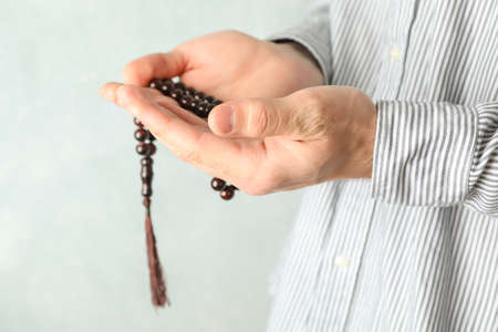 Man hold prayer beads in hands against grey background