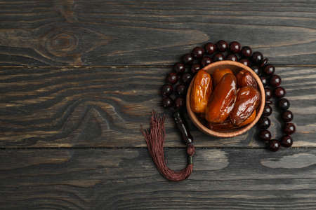 Wooden bowl with dates and prayer beads on wooden background, space for textの写真素材