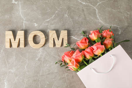 Gift bag with bouquet of orange roses and inscription Mom on brown background, top viewの写真素材