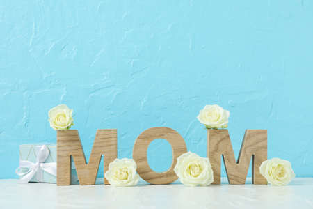 Inscription Mom with white roses on pink table against color background, space for textの写真素材