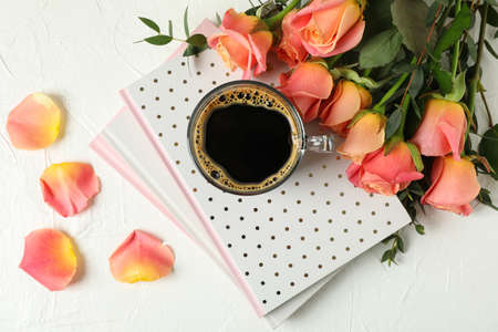 Composition with cup of coffee, notebooks and pink roses on white background, top viewの写真素材