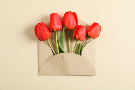 Envelope and beautiful red tulips with space for text on color background, top view