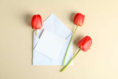 Envelope with space for text  and beautiful red tulips on color background, top view