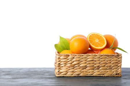 Wicker basket with ripe oranges on wooden table isolated on white background. Citrus food