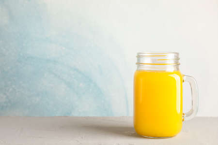Glass jar with fresh orange juice on white table against color background, space for text. Fresh natural drinkの写真素材