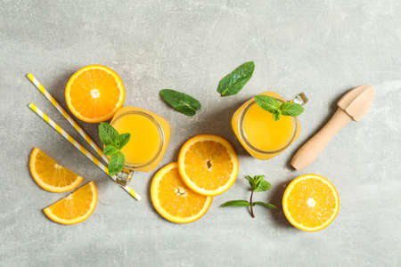 Flat lay composition with orange pieces, mint, tubules, wooden juicer and glass jars with fresh orange juice on grey background, space for text. Fresh natural drinksの写真素材